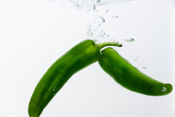 Two jalapeno peppers on white background in water with bubbles.