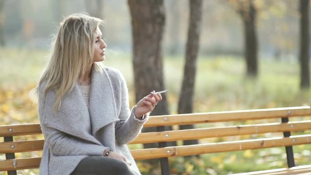 young beautiful business woman smoking a cigarette in the park. Autumn background 