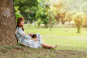 Pretty asian girl in vintage dress sitting leaning against on the tree relaxing.Vintage tone.