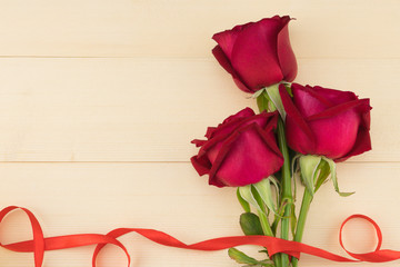 Red roses bouquet decorated with wave red ribbon on light wood background with copy space