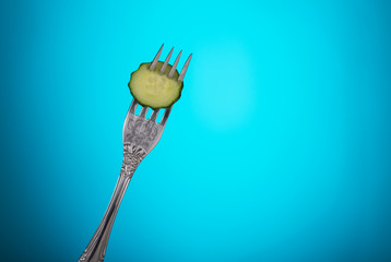 fork with a slice of cucumber on blue background close-up