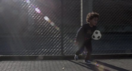 Cute little African American black kid playing with soccer ball in the field, urban background. 4K UHD