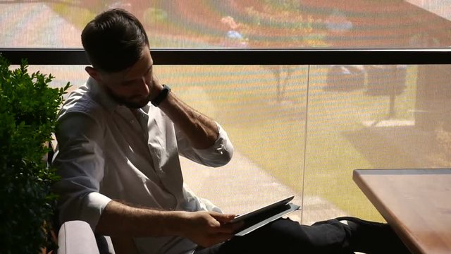 Cryptologist using tablet at cafe table and wipes sweat with tissue.