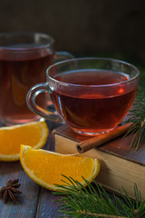 Tea in a glass mug, cinnamon stick, orange and fir branch.