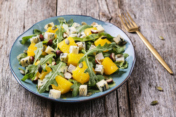 Baked pumpkin, blue cheese, arugula and nuts warm salad on turquoise plate on vintage wooden table. Healthy vegetarian food. Selective focus 