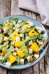 Baked pumpkin, blue cheese, arugula and nuts warm salad on turquoise plate on vintage wooden table. Healthy vegetarian food. Selective focus 