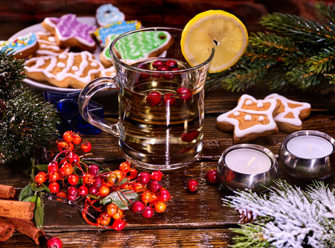 Christmas Tea cup glass and multicolored cookies on form stars on plate with fir branches. Mug decoration lemon slice on wooden table. Xmas treats and candels.