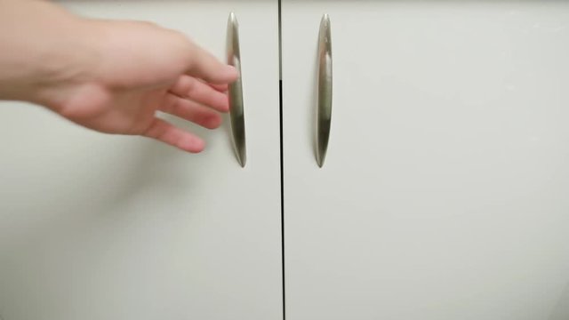 A hand opening a furniture door and throwing out rubbish into a dustbin. Close-up shot