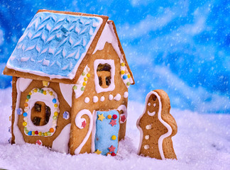 Gingerbread man side view, close-up. Ginger bread house standing in snow snowfall. Cookies with...