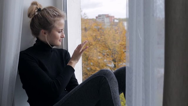 Sad young woman sitting on windowsill and looking at window