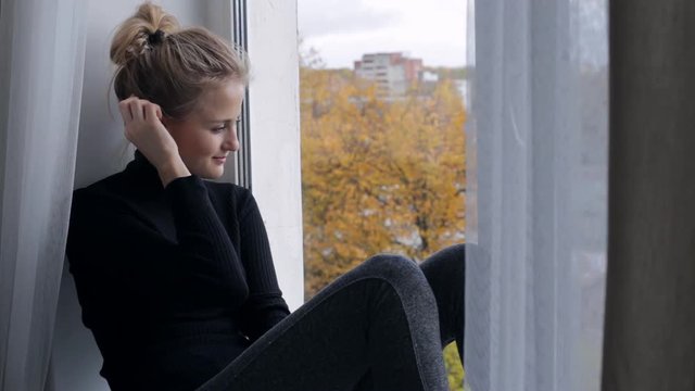 Sad woman looking at window and sitting on windowsill