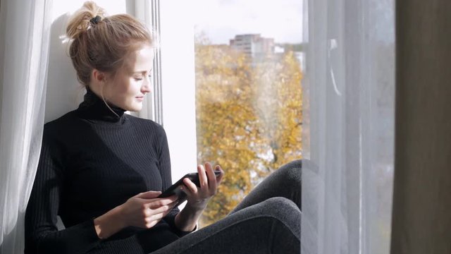 Woman with e-book sitting on the windowsill