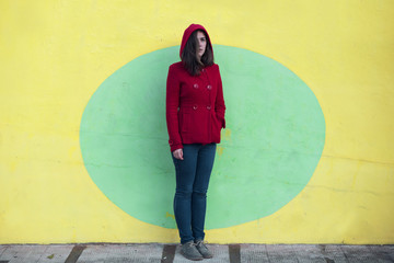 Retrato de mujer joven con chaqueta roja con capucha sobre pared de color amarillo y verde. Foto...
