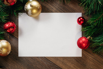 A frame of pine branches and Christmas decorations and A4 sheet of white paper on a wooden table....