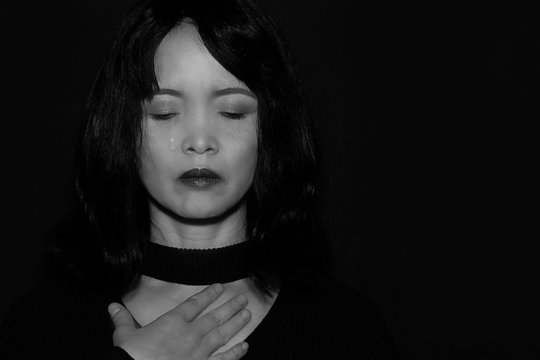 A close up portrait of a sad oriental woman on a black background	