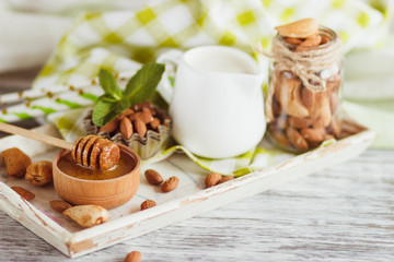 Honey in the wooden bowl, mint leaves, almonds and jar with milk on the wooden tray