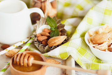Honey in the bowl, muesli, mint leaves, almonds and jar with milk on the wooden tray