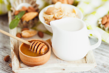 Honey in the bowl, muesli, mint leaves, almonds and jar with milk on the wooden tray