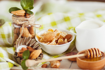 Honey in the bowl, muesli, mint leaves, almonds and jar with milk on the wooden tray