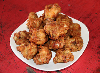 Pile of crispy fried chicken wings in the white dish on the red wooden table. fried chicken is a dish consisting of chicken pieces usually from broiler chickens and then pan fried.