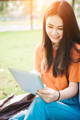 A young or teen asian girl student in university smiling and reading the book and look at the tablet or labtop computer in summer holiday.