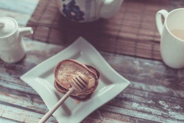 Delicious breakfast. Homemade Pancakes with honey and cup of tea on wooden rustic background table. Vintage style retro toned image