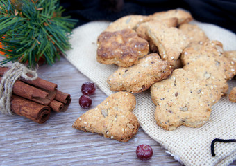 Homemade cookies with nuts on burlap. Cinnamon, pine branches and berries on wooden background. Christmas composition.