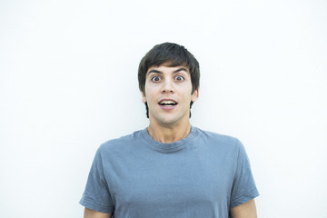 Fototapeta premium Retrato frontal de hombre con cabello castaño y camiseta gris sobre fondo blanco con expresión de asombro, sorpresa.