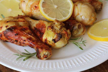 Grilled chicken legs with mustard on wooden table served on white plate with rosemary. BBQ dinner background