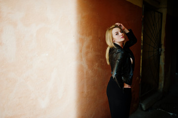 Fototapeta premium Elegant blonde girl wear on black leather jacket posing at streets of town background old wall with shadows.