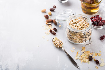Ingredients for homemade oatmeal granola in glass jar. Oat flakes, honey, raisins and nuts. Healthy breakfast concept with copy space.