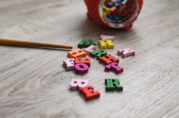 Multicolored letters of the alphabet, container for letters, and a school pointer made of wood on a wooden background