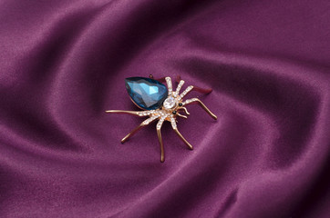 Golden spider with a big blue stone on silk fabric