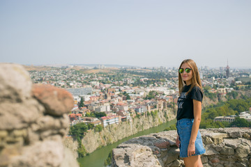 The girl is beautiful. On the background of the city. The view from the top. panorama. A stone fence. Old Tbilisi