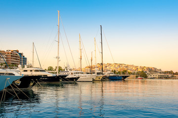 Fototapeta na wymiar Sailing and luxury motor yachts in marina of Zeas. Sunset and view of Kastela in the background. Piraeus city, Greece