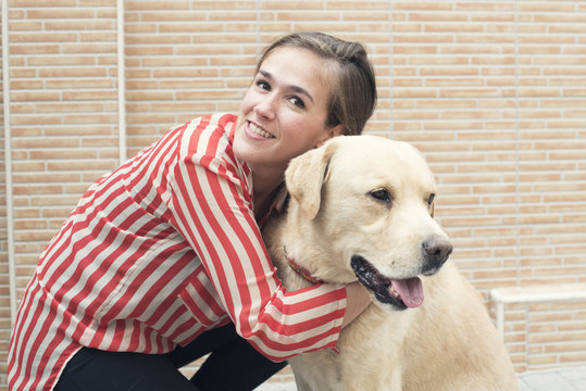 Retrato de chica con camisa de rayas abrazando a un perro labrador