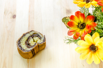 Sweet roll cake and beautiful cloth artificial flowers on wooden background
