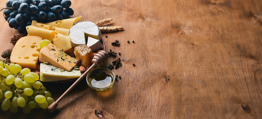A bottle of wine, and a large assortment of cheeses, honey, nuts and spices, on a wooden table. Top view. Free space for text.