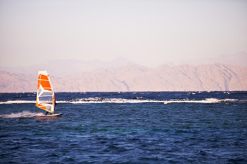 Sportman windsurfer on the sea surface against mountains at sunset time