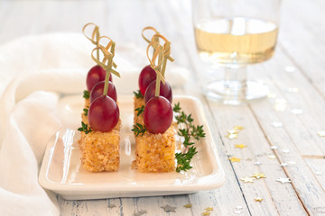 Canape with pink grapes and cheese in a nut breaded, on wooden skewers. Festive snack on a white plate on a light blue wooden background, selective focus