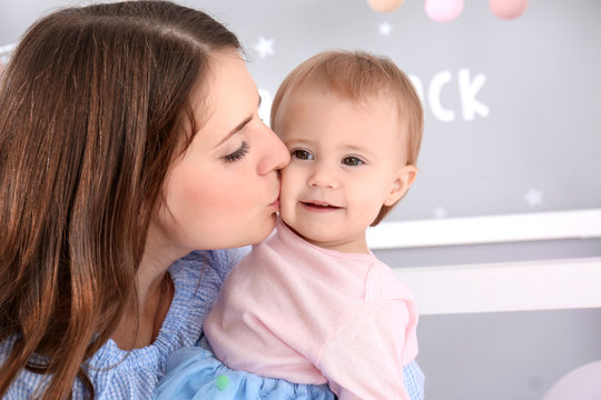 Young mother kissing cute baby at home