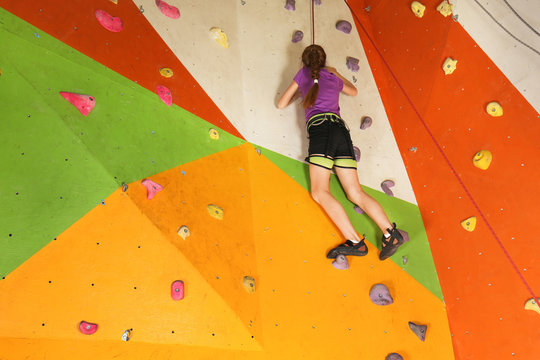 Cute little girl climbing on wall in gym