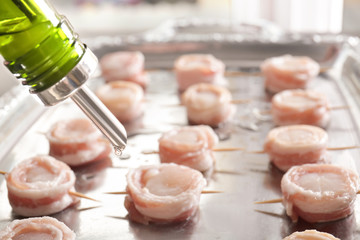 Adding oil to raw bacon wrapped scallops on metal tray