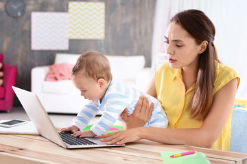 Fototapeta na wymiar Young mother holding baby while working in home office