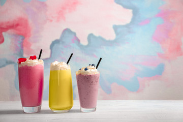 Different milkshakes in glasses on table against color background