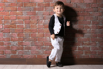 Adorable little boy standing near brick wall