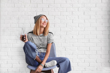 Attractive hipster girl on chair against white brick wall