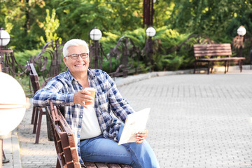 Fototapeta premium Handsome mature man with coffee and newspaper in park
