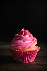 Yummy cupcake on wooden table against dark background
