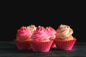 Yummy cupcakes on wooden table against dark background